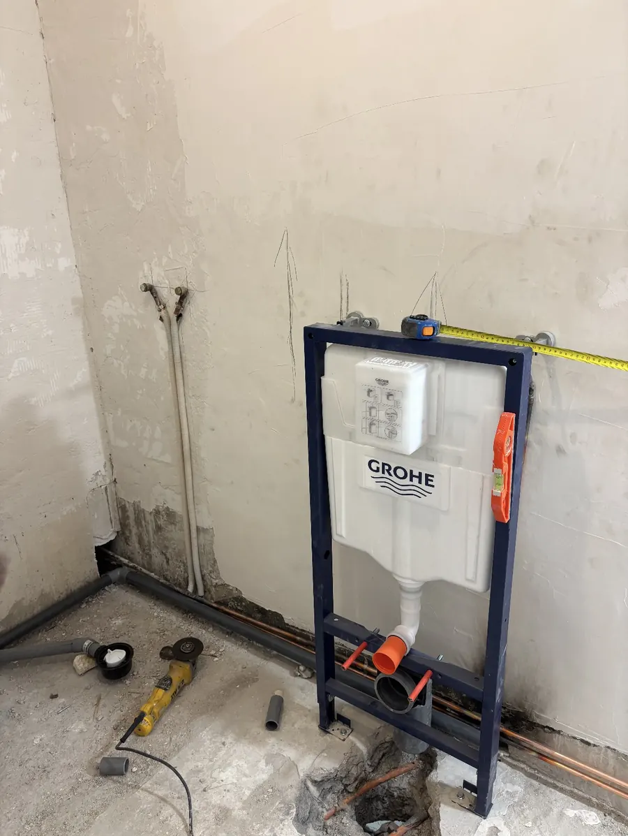 Chantier de plomberie en cours : bâti-support de WC Grohe fixé au mur, évacuation raccordée au sol, arrivées d'eau en attente